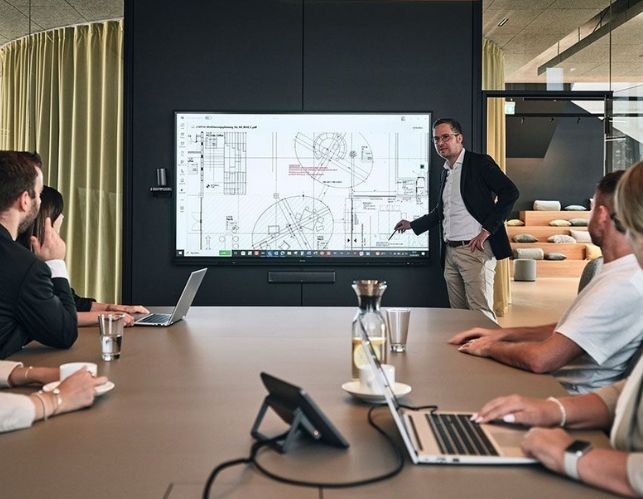 Mitarbeiter von Streit Service & Solution arbeiten zusammen in einem Besprechungsraum. Am Bildschirm wird etwas präsentiert