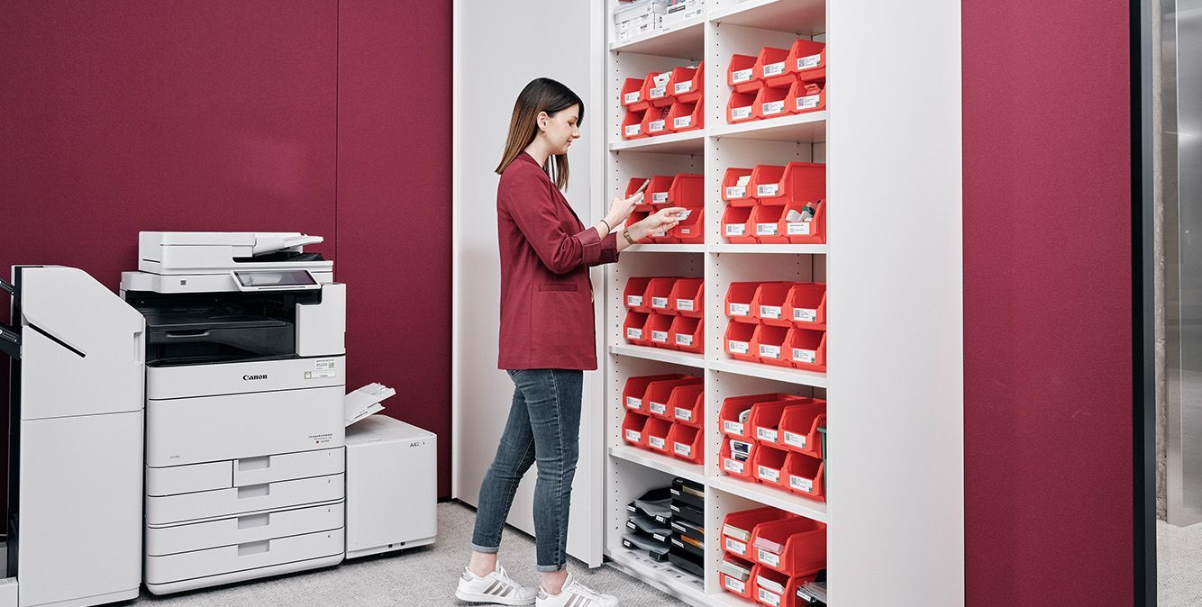 Frau steht vor Kanban-Regal und scannt Karte