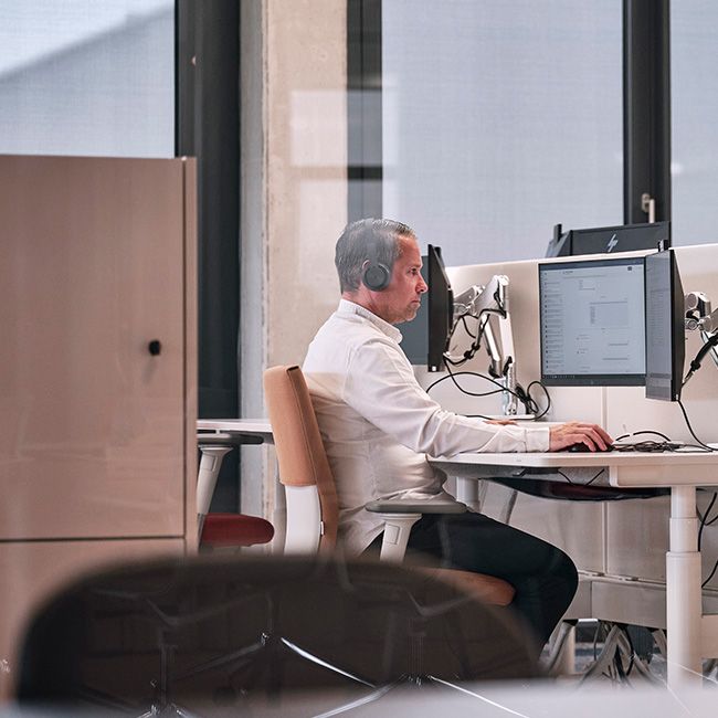 Mann arbeitet mit Headset an zwei Bildschirmen