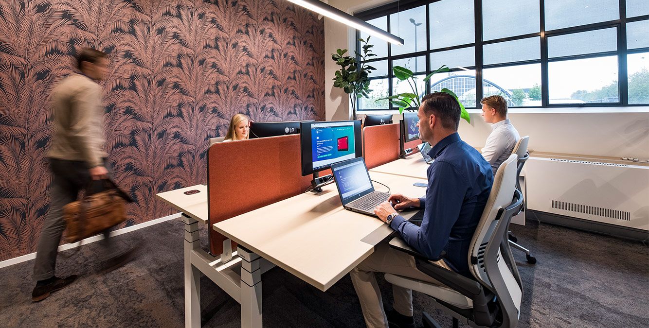 Personen sitzen an mehreren Arbeitsplätzen und arbeiten am Computer