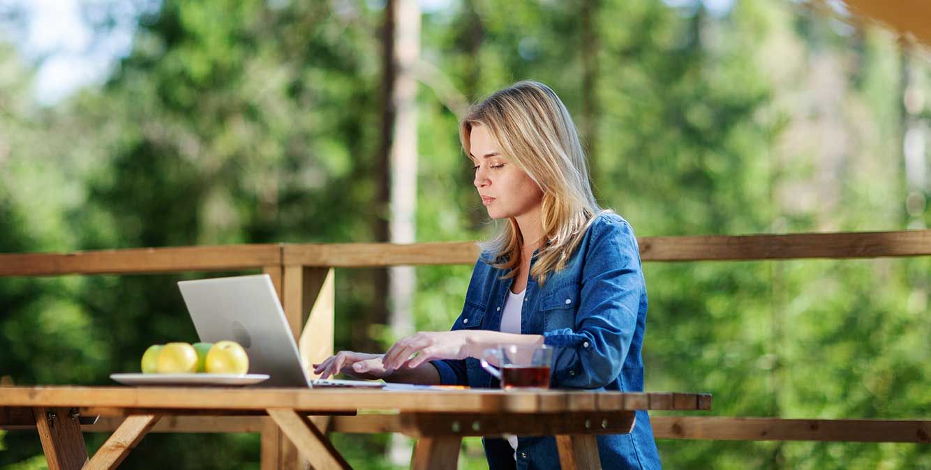 Frau sitzt draußen an einem Tisch und arbeitet am Laptop