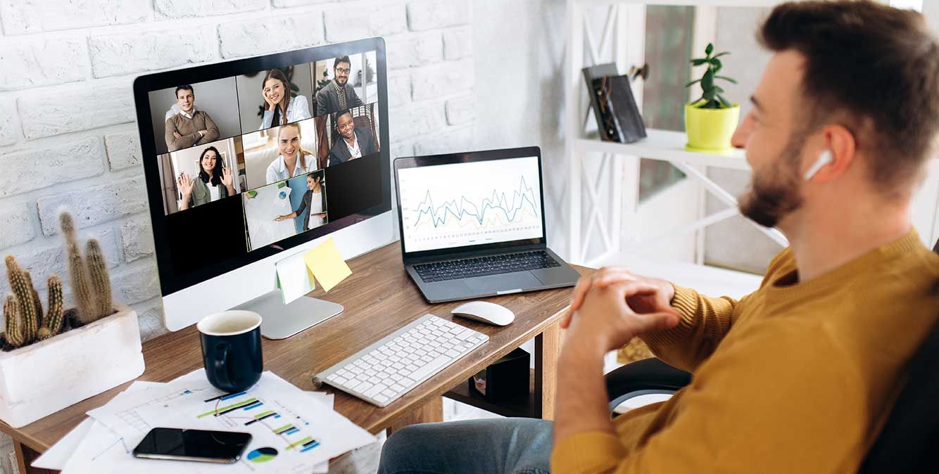 Ein Mann sitzt am Schreibtisch und spricht mit weiteren Personen per Videokonferenz