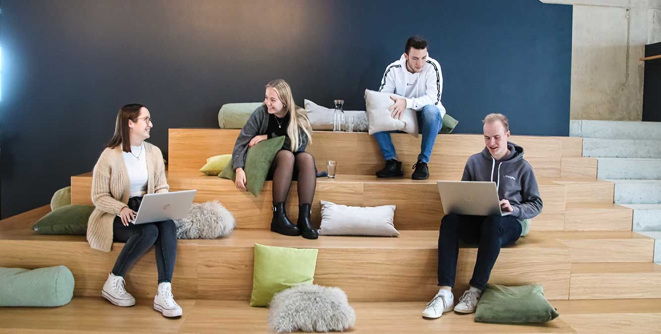 Mitarbeiter von Streit Service & Solution sitzen zusammen auf einer Treppe und sprechen miteinander.