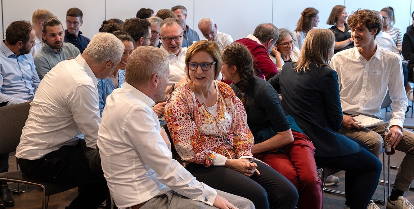 Mehrere Männer und Frauen sprechen auf einer Veranstaltung miteinander und lachen dabei.