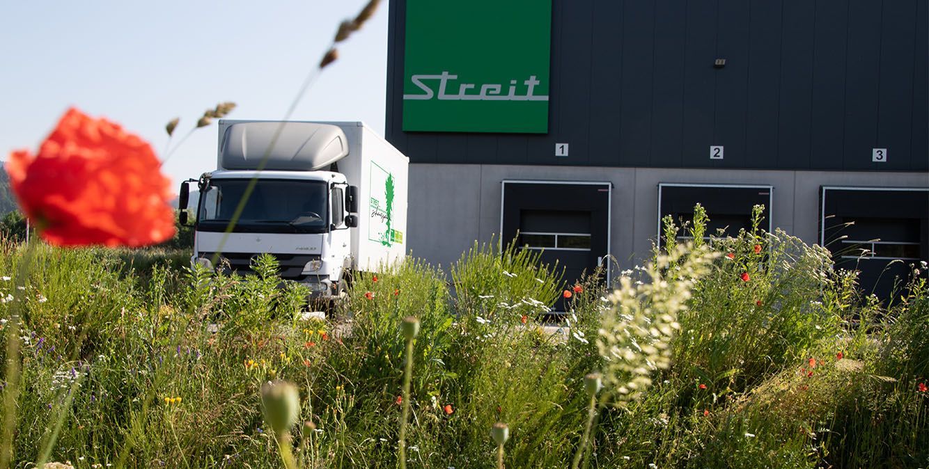 Wiese mit Blumen, dahinter ein weißer LKW und ein Gebäude mit dem Logo der Firma Streit Service & Solution