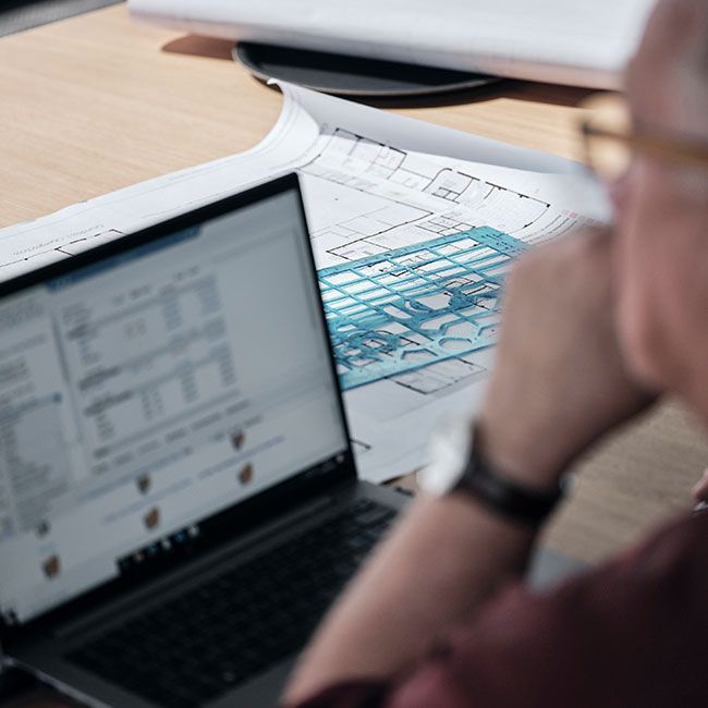 Mitarbeiter von Streit Service & Solution arbeitet am Laptop. Neben ihm auf dem Tisch liegt ein Plan einer Büros.
