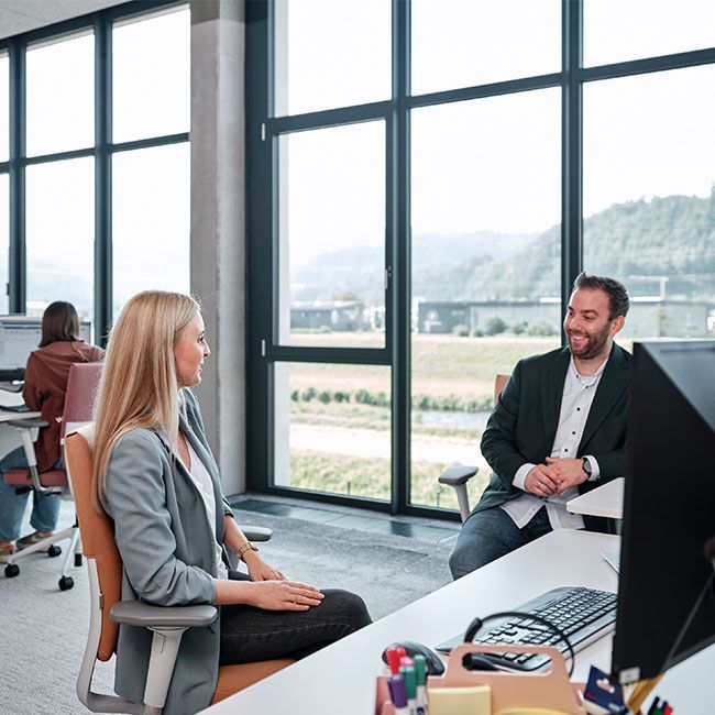 Mitarbeiter von Streit Service & Solution sitzen an ihrem Arbeitsplatz und sprechen miteinander