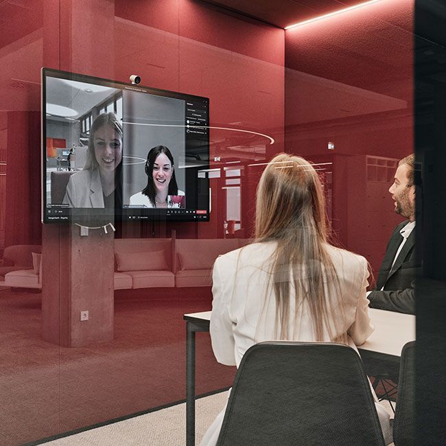 Mitarbeiter von Streit Service & Solution sitzen in einem Besprechungsraum und sprechen per Videokonferenz mit zwei Personen