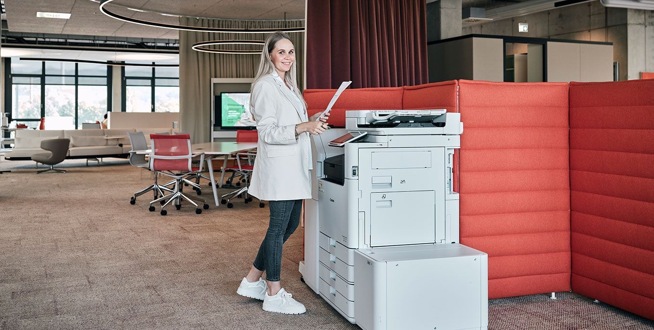 Mitarbeiterin von Streit Service & Solution steht einem Druckgerät und hält ein Papier in der Hand