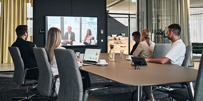 Mitarbeiter von Streit Service & Solution sitzen gemeinsam in einem Besprechungsraum und sprechen per Videokonferenz mit zwei weiteren Personen