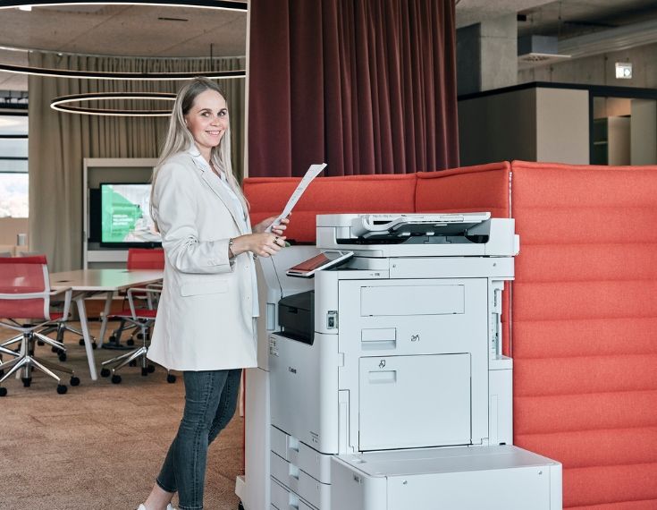 Mitarbeiterin von Streit Service & Solution steht einem Druckgerät und hält ein Papier in der Hand