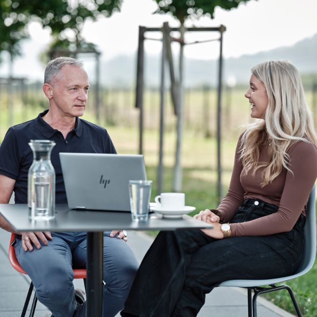 Zwei Personen sitzen draußen an einem Tisch und arbeiten am Laptop