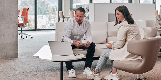 Mitarbeiter sprechen miteinander, trinken Kaffee und schauen gemeinsam in einen Laptop