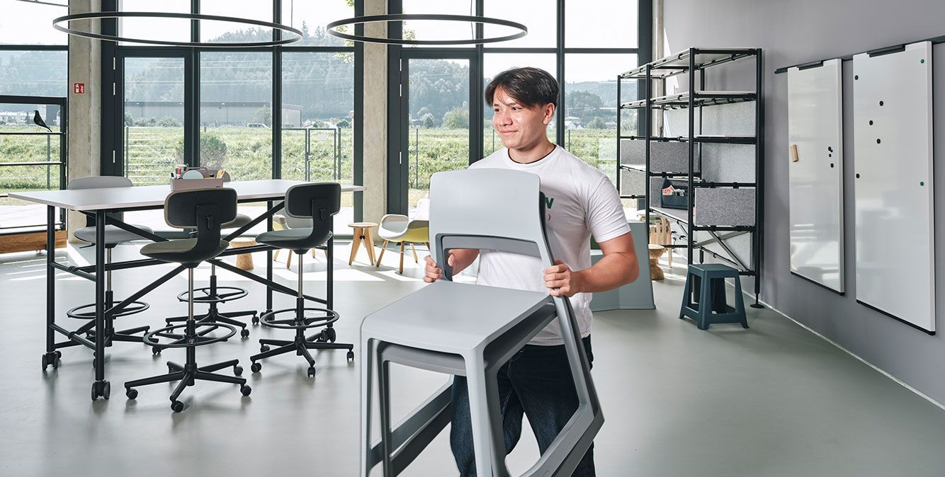 Auszubildender von Streit Service & Solution trägt Stühle durch das Büro