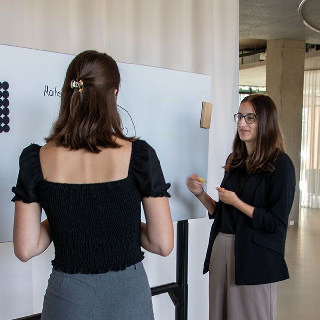 Zwei duale Studentinnen von Streit Service & Solution arbeiten zusammen an einem Whiteboard und sprechen miteinander