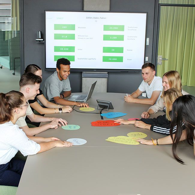 Auszubildende von Streit Service & Solution sitzen zusammen an einem Konferenztisch und sprechen miteinander