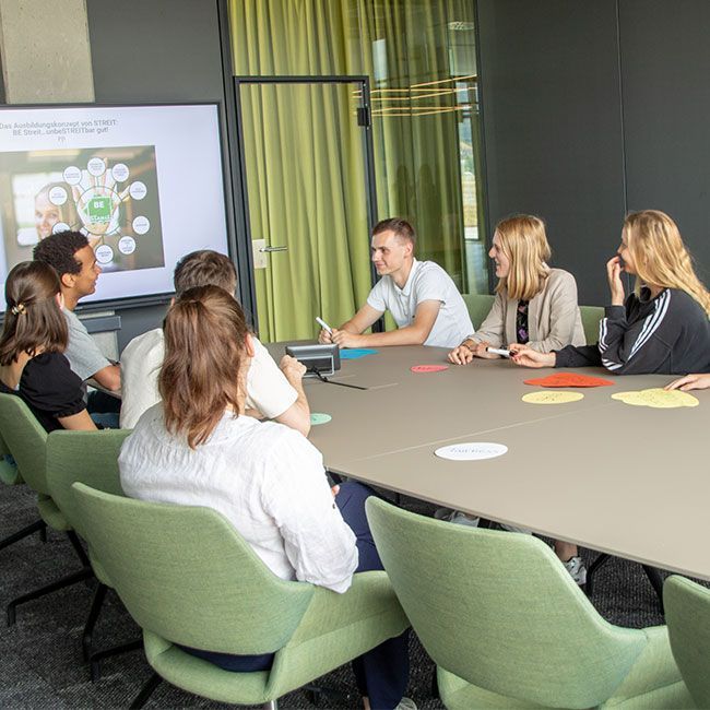 Duale Studenten von Streit Service & Solution sitzen zusammen in einem Besprechungsraum am Tisch und sprechen miteinander