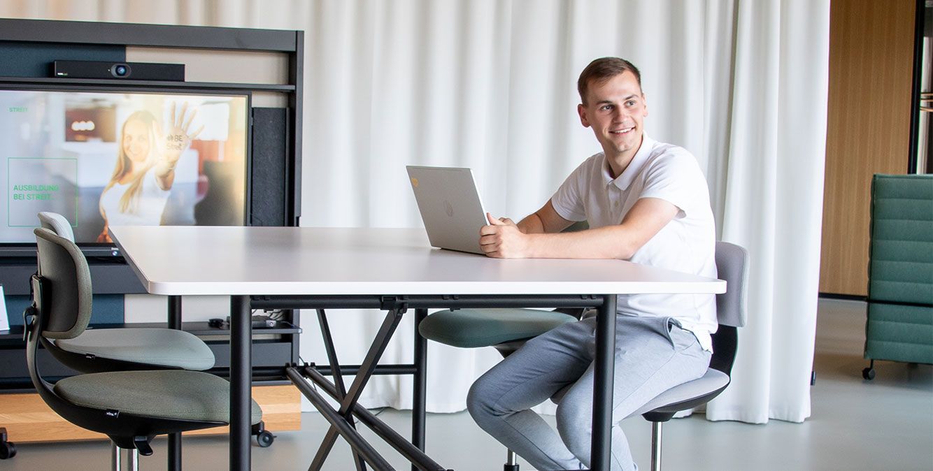 Dualer Student von Streit Service & Solution sitzt an einem Tisch und arbeitet am Laptop