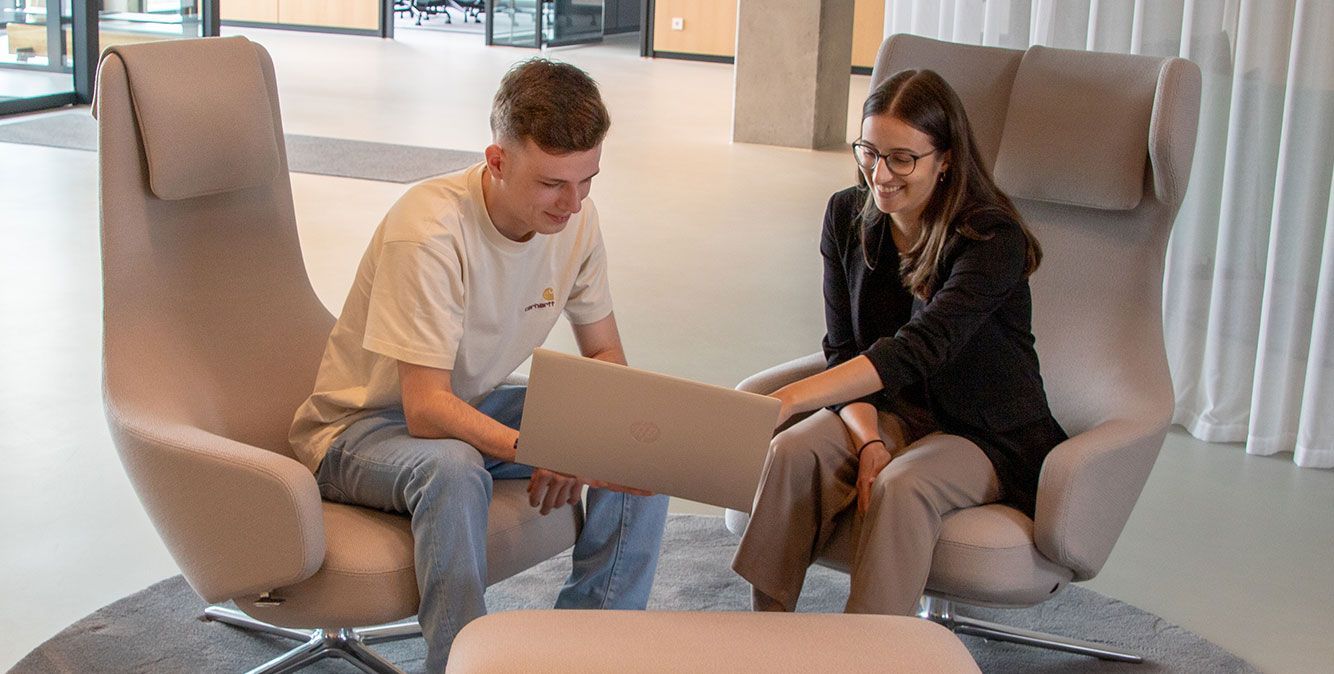 Zwei Duale Studenten von Streit Service & Solution sitzen auf zwei Sesseln und schauen zusammen auf einen Laptop