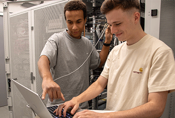 Zwei Auszubildende von Streit Service & Solution arbeiten im Serverraum und am Laptop
