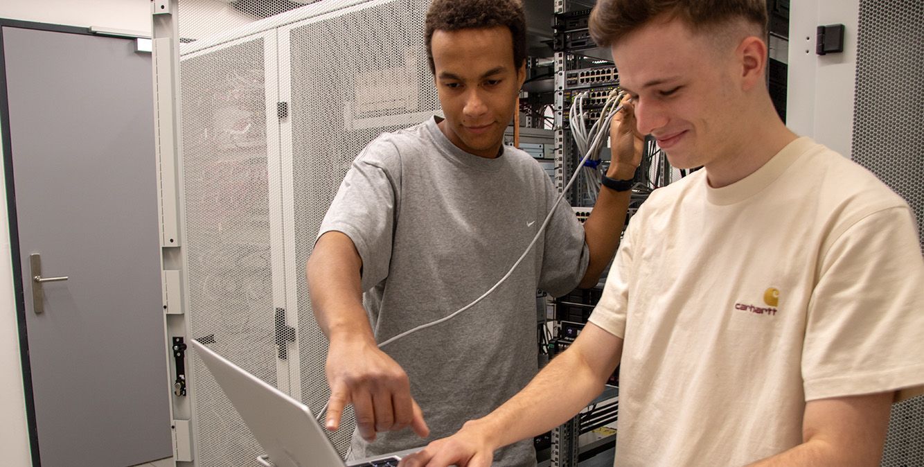 Zwei Auszubildende von Streit Service & Solution arbeiten im Serverraum am Server und am Laptop
