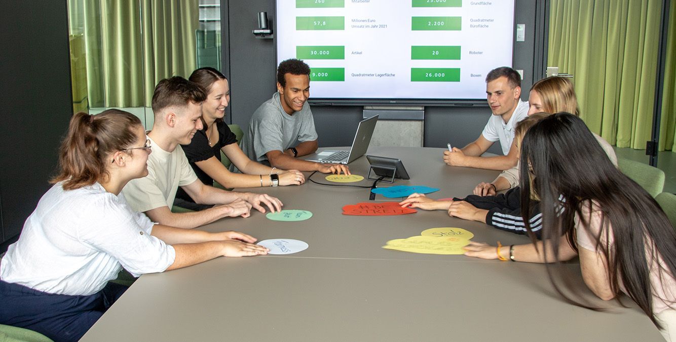 Schülerpraktikanten bei Streit Service & Solution sitzen zusammen an einem Tisch und sprechen miteinander