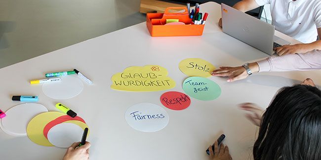 Studenten sitzen an einem Tisch auf dem buntes Papier und Stifte liegen