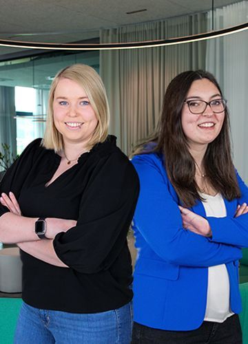 Zwei lächelnde Frauen stehen Rücken an Rücken in einer Arbeitswelt