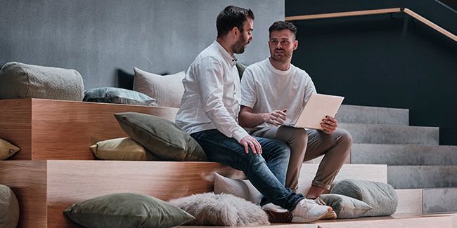 Mitarbeiter von Streit Service & Solution sitzen zusammen auf einer Treppe und arbeiten an einem Laptop