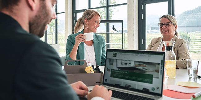 Im Vordergrund bestellt ein Mann im Onlineshop von Streit Service & Solution. Im Hintergrund sitzen zwei Frauen und lachen.