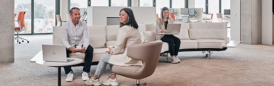 Drei Mitarbeiter von Streit Service & Solution sitzen auf einem Sofa und arbeiten. Zwei sprechen miteinander und eine weitere arbeitet am Laptop