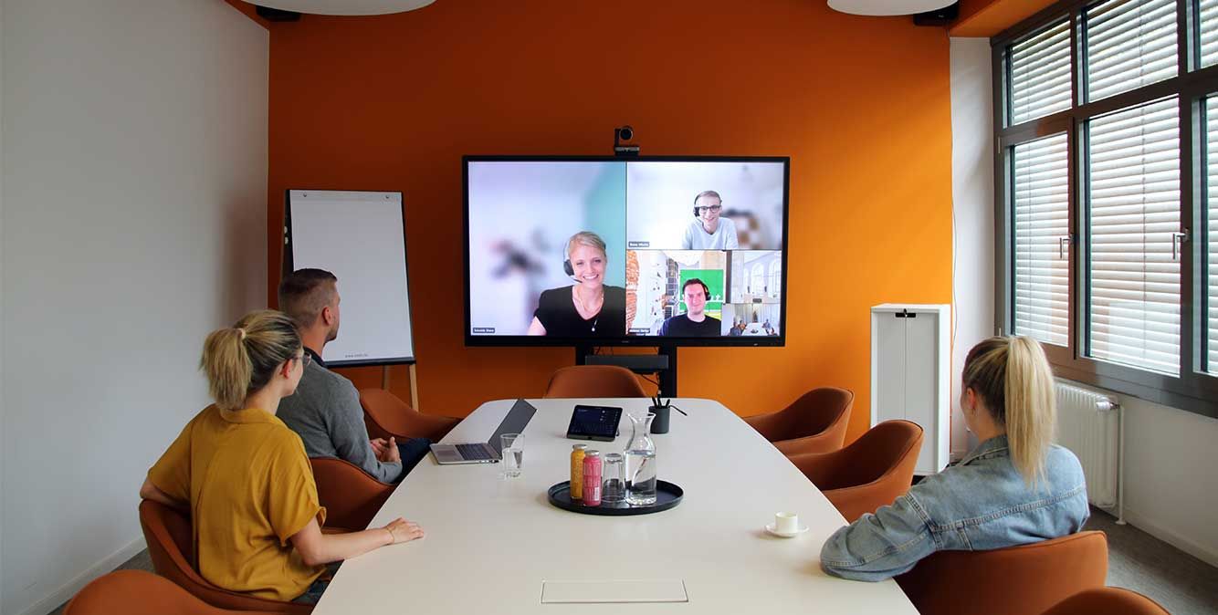 Mitarbeiter von Streit Service & Solution sitzen zusammen in einem Konferenzraum und sprechen per Videokonferenzsystem mit weiteren Personen